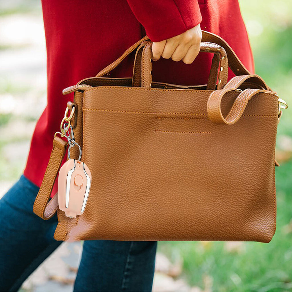 Brown leather handbag held by a person wearing a red sweater and blue jeans, with a blurred green outdoor background.