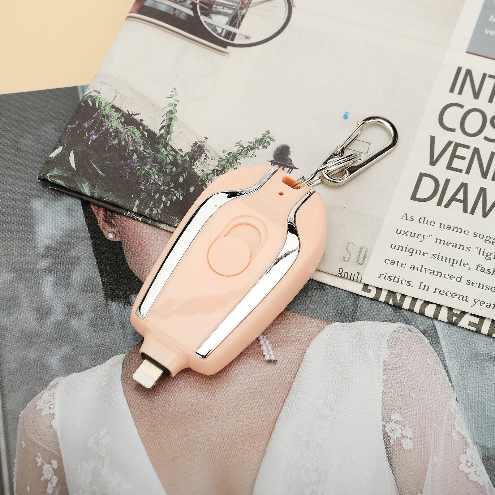 Person wearing a peach-colored air pod case with a keychain on a magazine background